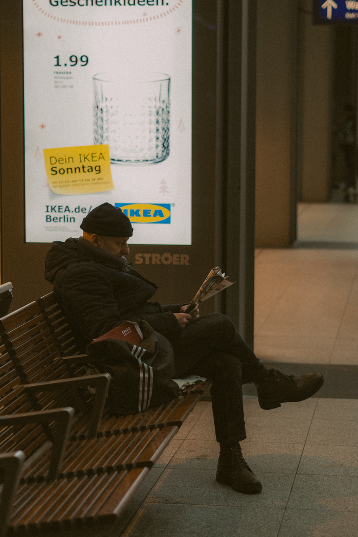 Home Adult man sitting and reading a newspaper beside an IKEA ad in urban Berlin setting.